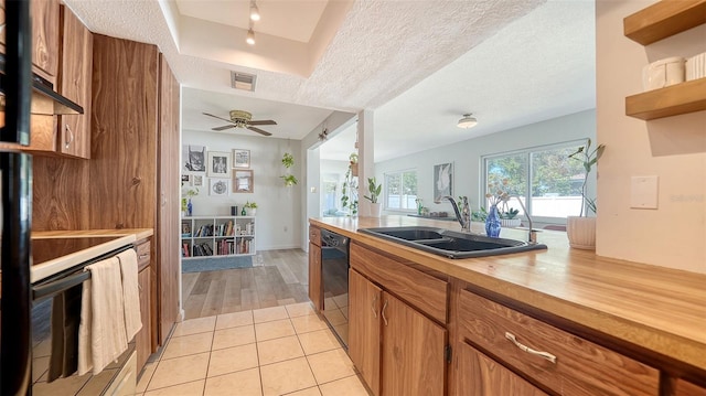 kitchen with light tile patterned floors, a tray ceiling, a sink, dishwasher, and brown cabinets