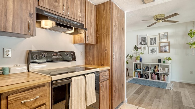 kitchen featuring electric range oven, light wood-style floors, under cabinet range hood, a textured ceiling, and brown cabinets