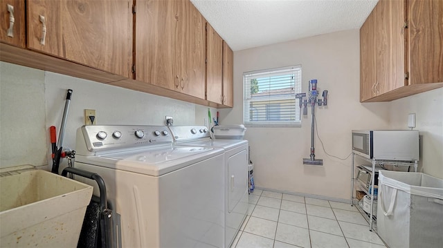 laundry area with a sink, a textured ceiling, cabinet space, light tile patterned floors, and washing machine and clothes dryer