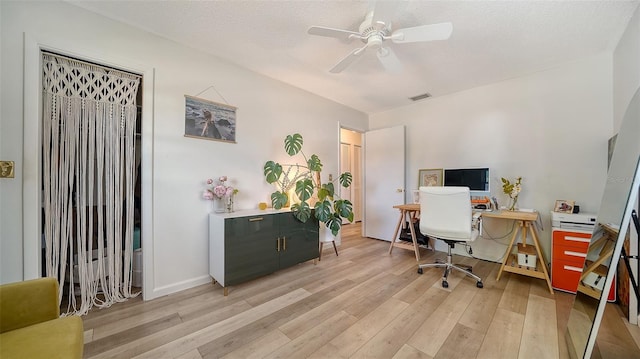 office space with baseboards, visible vents, ceiling fan, light wood-style floors, and a textured ceiling