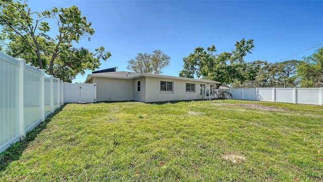 back of property with a gate, a yard, a fenced backyard, and stucco siding