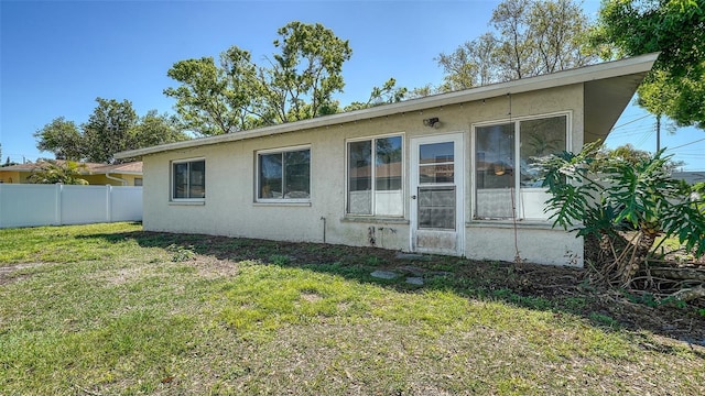 rear view of house with a yard, stucco siding, and fence