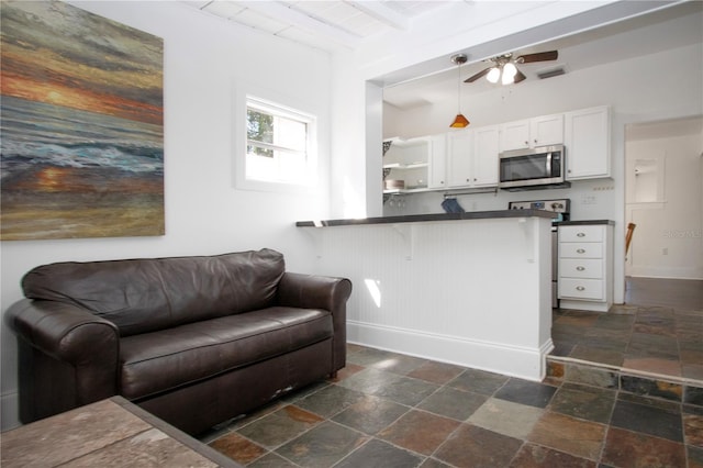 living area featuring beamed ceiling, stone tile flooring, baseboards, visible vents, and a ceiling fan