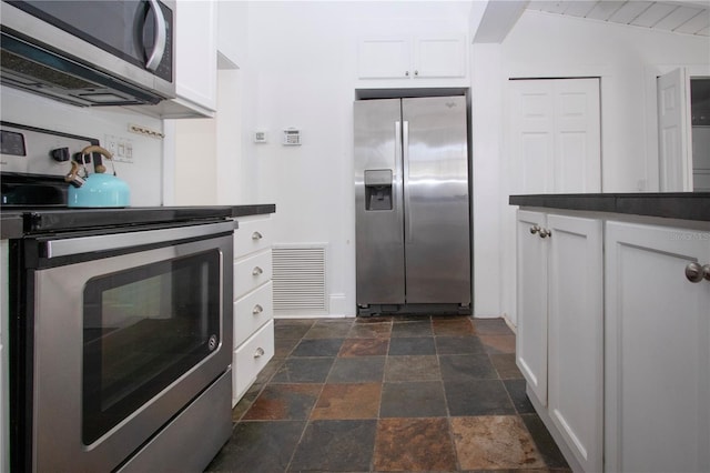 kitchen featuring stainless steel appliances, stone tile flooring, dark countertops, white cabinetry, and visible vents