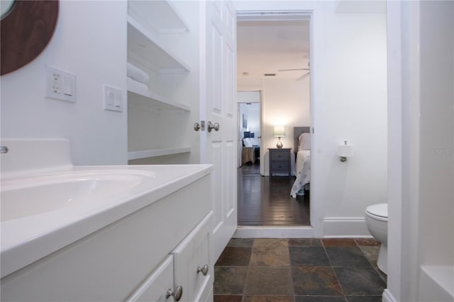 bathroom with stone finish floor, connected bathroom, ceiling fan, toilet, and vanity