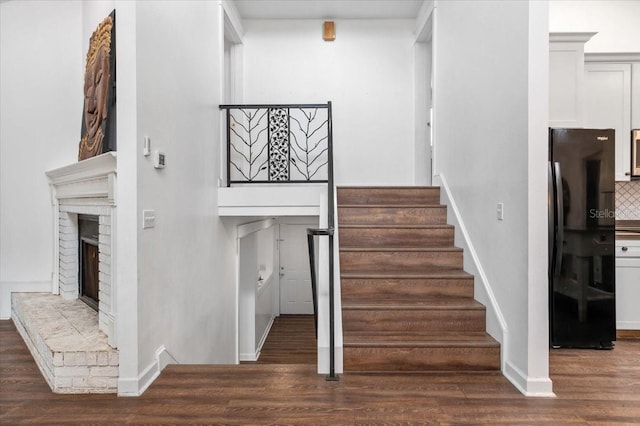 staircase with a brick fireplace, wood finished floors, and baseboards