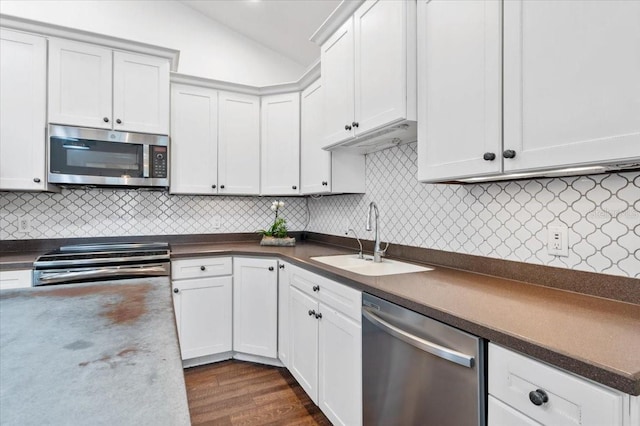 kitchen with dark countertops, dark wood finished floors, vaulted ceiling, stainless steel appliances, and a sink