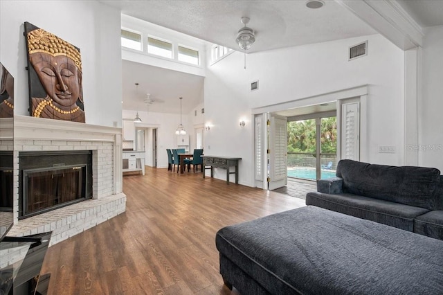 living room with wood finished floors, visible vents, beam ceiling, ceiling fan, and a brick fireplace