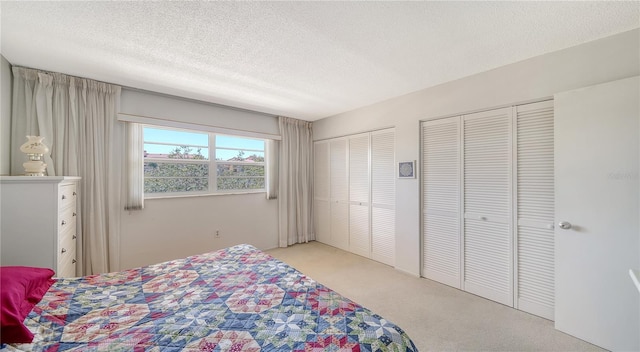bedroom featuring light carpet, a textured ceiling, and two closets
