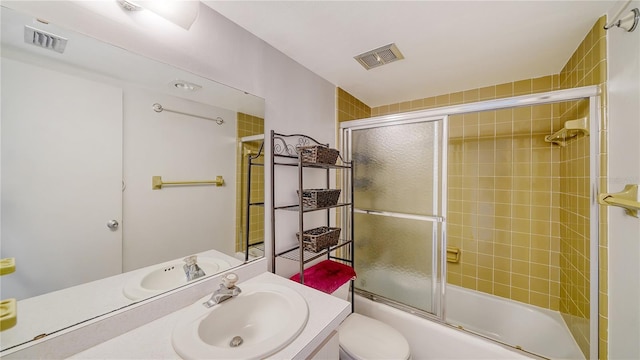 bathroom with toilet, vanity, visible vents, and combined bath / shower with glass door