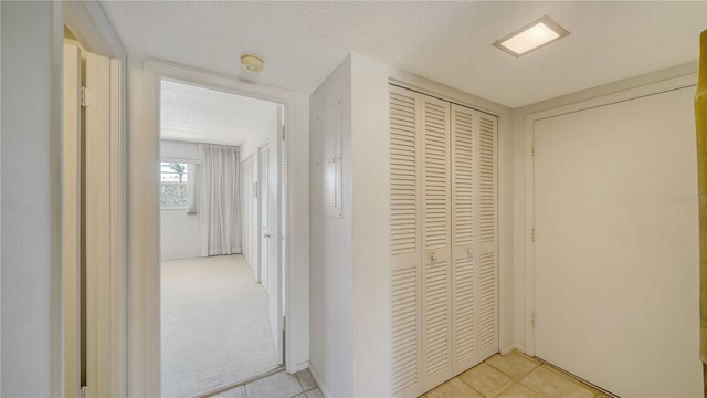 corridor featuring a textured ceiling, light carpet, and light tile patterned floors