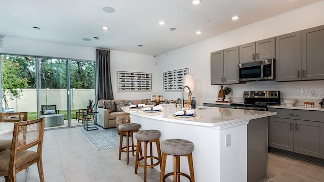 kitchen with an island with sink, gray cabinets, a sink, light countertops, and appliances with stainless steel finishes