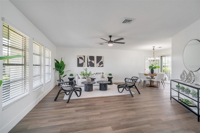 living area with ceiling fan with notable chandelier, wood finished floors, visible vents, and baseboards