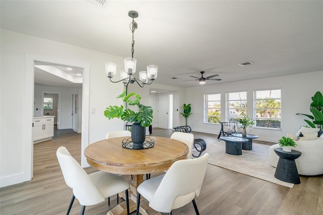 dining area with ceiling fan with notable chandelier, light wood-style floors, visible vents, and baseboards