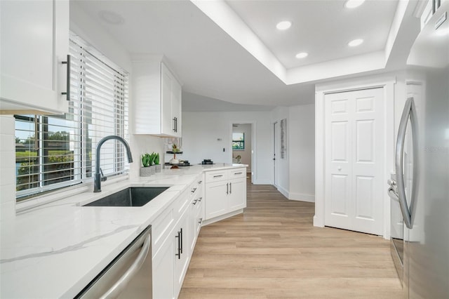 kitchen with light stone countertops, appliances with stainless steel finishes, light wood-style floors, white cabinetry, and a sink