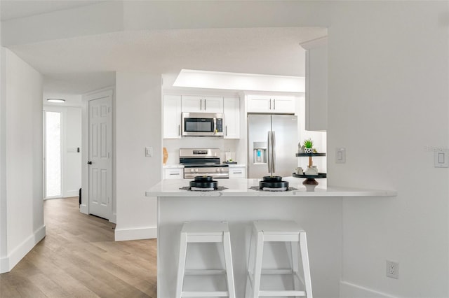 kitchen featuring light wood-style flooring, white cabinetry, a peninsula, appliances with stainless steel finishes, and light countertops