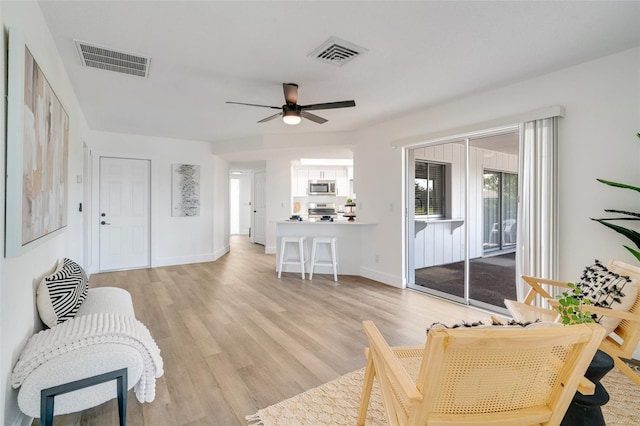 living area featuring light wood finished floors, visible vents, baseboards, and a ceiling fan