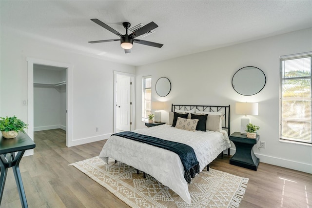 bedroom featuring a walk in closet, wood finished floors, baseboards, and a textured ceiling