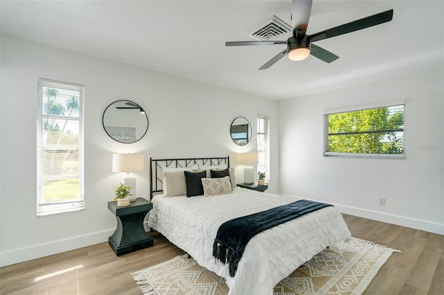 bedroom with ceiling fan, wood finished floors, visible vents, and baseboards