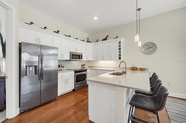 kitchen with a sink, a peninsula, white cabinetry, and stainless steel appliances