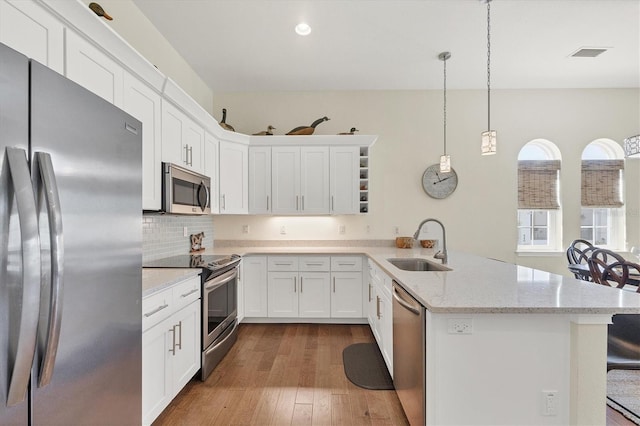 kitchen with light stone counters, wood finished floors, a peninsula, a sink, and stainless steel appliances