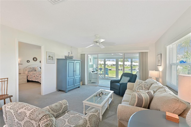 living area with a textured ceiling, light colored carpet, and ceiling fan