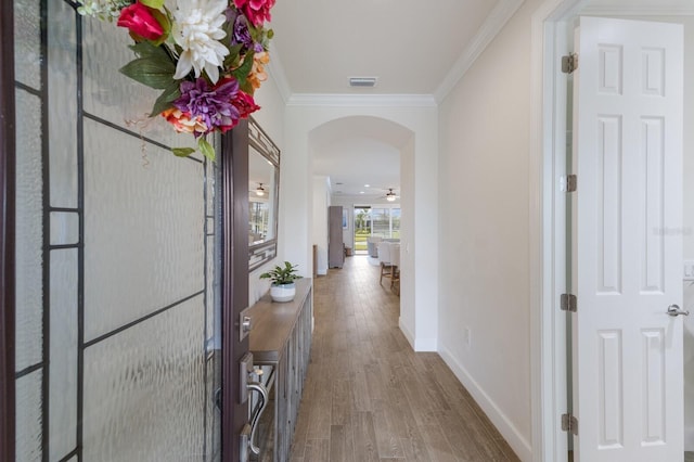 corridor featuring visible vents, ornamental molding, wood finished floors, arched walkways, and baseboards