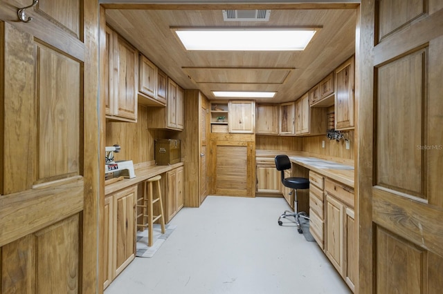 home office featuring wood walls, visible vents, concrete floors, and built in study area