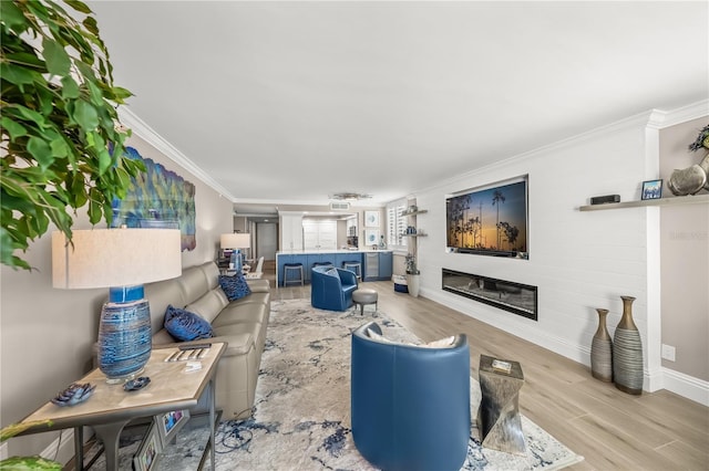 living room featuring a glass covered fireplace, baseboards, crown molding, and light wood-style floors