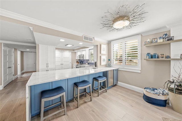 kitchen featuring visible vents, ornamental molding, a peninsula, stainless steel appliances, and white cabinetry