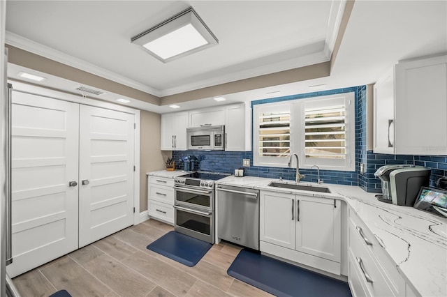 kitchen with visible vents, crown molding, stainless steel appliances, white cabinetry, and a sink