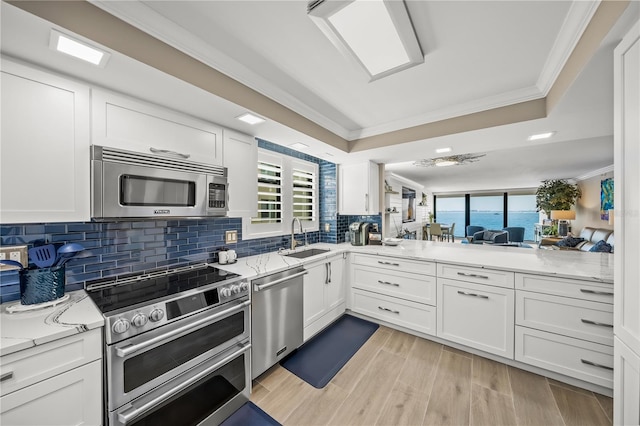 kitchen with a sink, appliances with stainless steel finishes, white cabinets, and crown molding