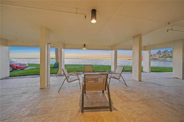 patio terrace at dusk featuring a lawn and a water view