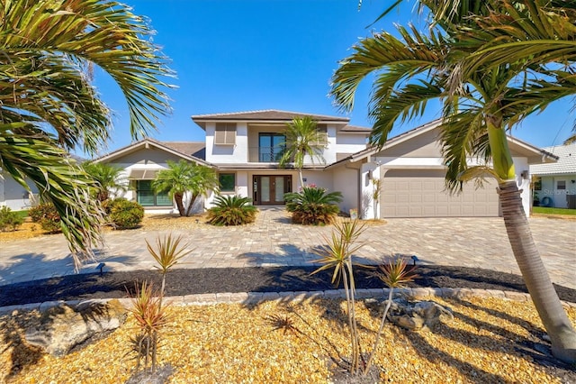 view of front facade with decorative driveway, french doors, an attached garage, and stucco siding