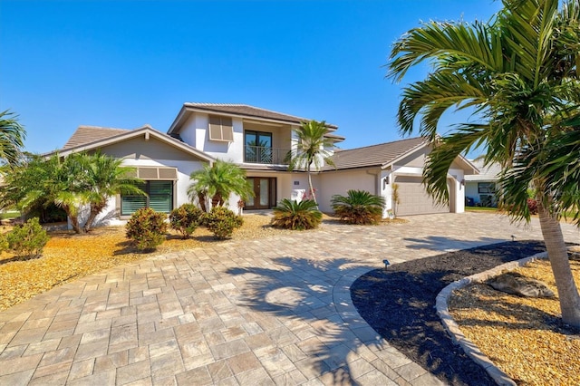 view of front of home with a tile roof, stucco siding, decorative driveway, a garage, and a balcony