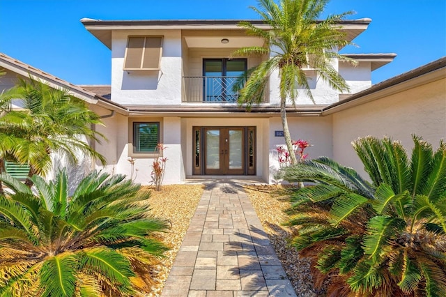 view of exterior entry featuring a balcony, french doors, and stucco siding