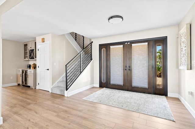 foyer entrance with beverage cooler, french doors, light wood finished floors, baseboards, and stairs