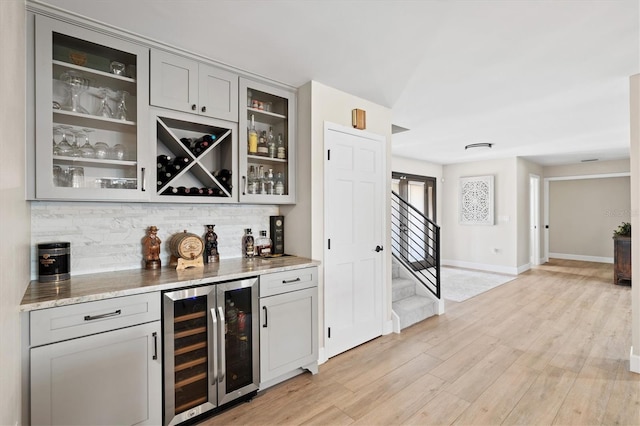 bar with stairway, beverage cooler, light wood-type flooring, a dry bar, and tasteful backsplash