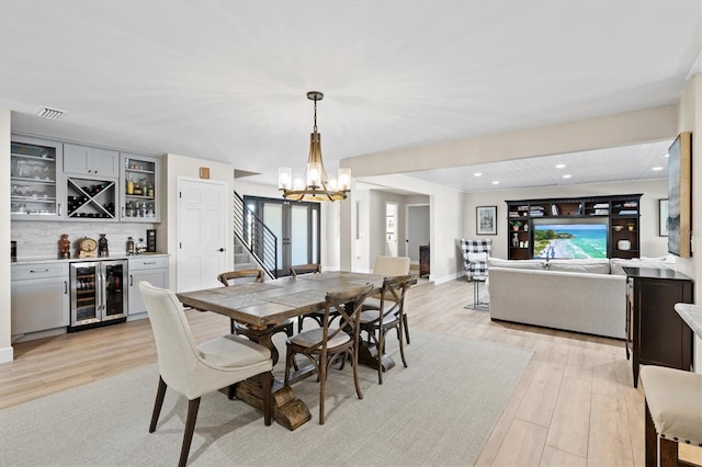 dining space with light wood-type flooring, visible vents, beverage cooler, an inviting chandelier, and a dry bar