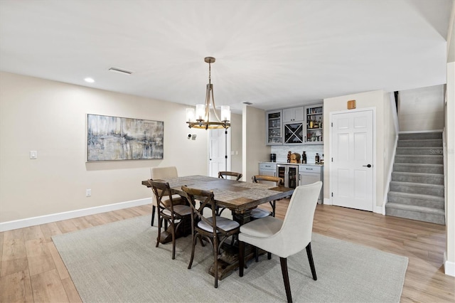 dining area with baseboards, a dry bar, stairs, light wood-style flooring, and a notable chandelier