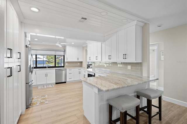 kitchen featuring light wood-style floors, backsplash, appliances with stainless steel finishes, and a peninsula