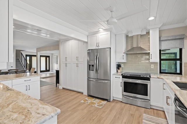 kitchen with backsplash, light wood-style flooring, appliances with stainless steel finishes, and wall chimney exhaust hood