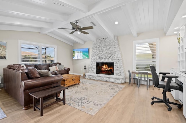 living room with a wealth of natural light, a stone fireplace, light wood-style flooring, and ceiling fan