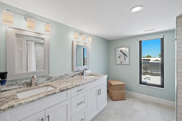 full bath featuring a sink, baseboards, double vanity, and tile patterned flooring