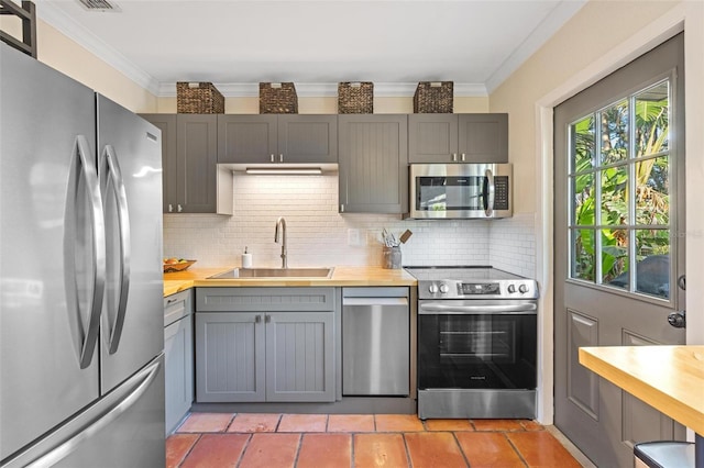 kitchen featuring gray cabinets, ornamental molding, a sink, appliances with stainless steel finishes, and butcher block counters