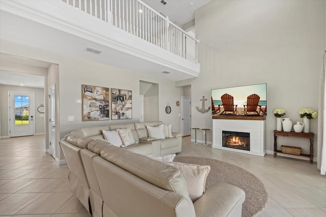 living room featuring visible vents, baseboards, light tile patterned floors, a high ceiling, and a glass covered fireplace