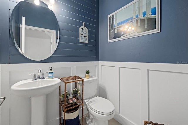 half bathroom with a sink, a wainscoted wall, toilet, and a decorative wall