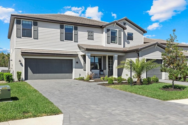 traditional-style house featuring an attached garage, covered porch, stucco siding, a front lawn, and decorative driveway