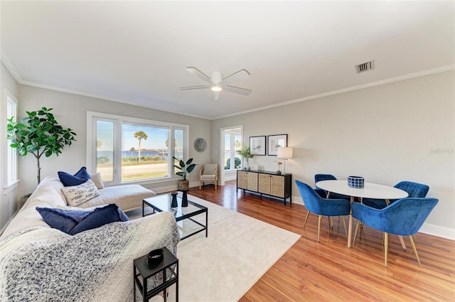 living area featuring a ceiling fan, wood finished floors, visible vents, baseboards, and crown molding