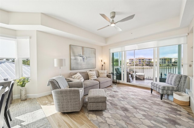 living area with a ceiling fan, a raised ceiling, wood finished floors, and baseboards